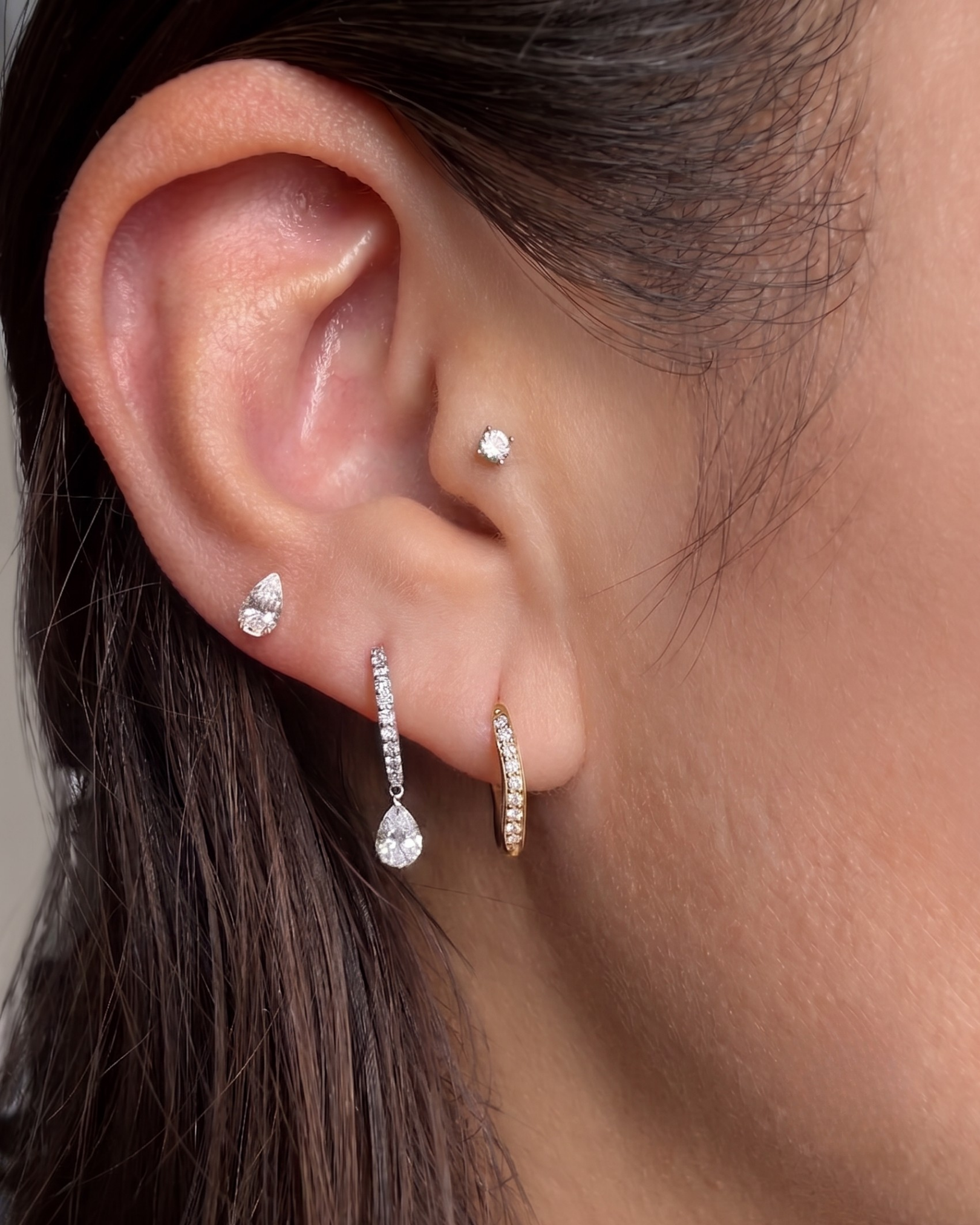 Close-up of a model's ear wearing the Floating Pear Diamond Stud, styled with other diamond hoop and stud earrings.